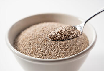 Wall Mural - White chia seeds in a white bowl set against a white background. Scooping with a stainless steel spoon.