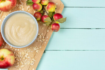 Wall Mural - Oatmeal porridge for the baby from ground cereals in a blue bowl, red ripe apples on a wooden board on a blue background. Space for text. Baby nutrition, the first complementary feeding of a child.