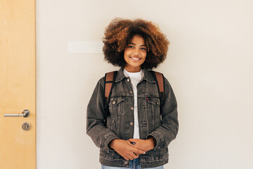 Wall Mural - Teenage girl in casuals standing at wall in school and looking at camera