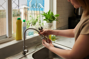 Hands of woman with wrench removing kitchen tap to attach aerator head