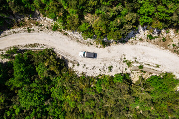 Aerial of Offroad truck driving on a narrow mountain road through the forest