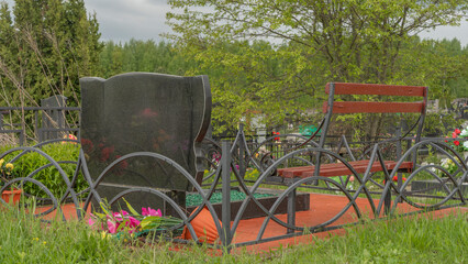 Headstone with a bench next to it. City geaveyard. City cemetery with fresh graves.