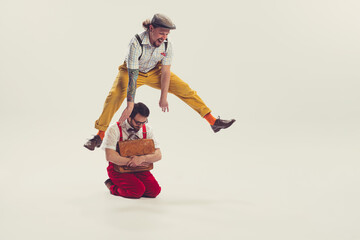 Two cheerfull dudes, young men in old-school fashioned attire running, jumping, having fun isolated on white background. Vintage, retro style concept