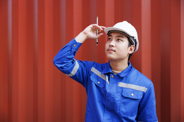 young asian engineer wearing the white safety helmet with red container background. concept : logistic man working in import-export yard.