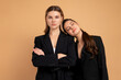 © Andrii - Two young business woman dressed black suit standing studio orange color background