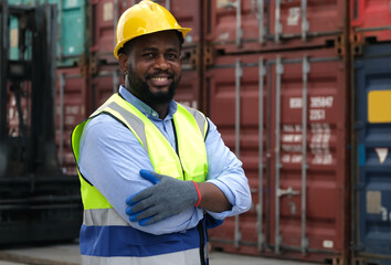 Black worker wearing hard hat looking at camera and cross his arms  with background of cargo containers.