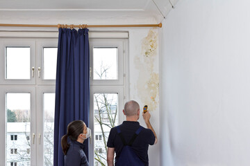 Woman watching a man measuring the temperature of an external wall where mildew is growing with an infrared or laser thermometer.