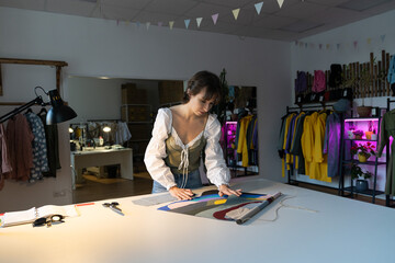 Wall Mural - Woman dressmaker work late in studio choosing fabric samples for new clothes collection sewing. Female designer stay in workshop late busy with brand and small business development. Atelier ownership