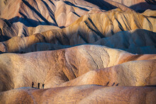 Three Hikers Emerge Along A Ridge Of The Desert Badlands Found At Zabriksie Point In Death Valley, California, USA.