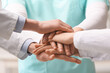 © Pixel-Shot - Group of doctors putting hands together in clinic, closeup