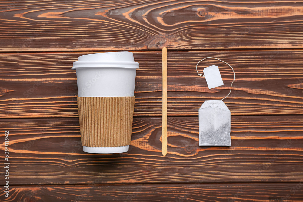 Takeaway paper cup, spoon and tea bag on wooden background