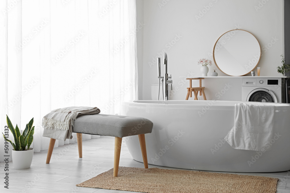 Interior of light room with soft bench, bathtub and washing machine