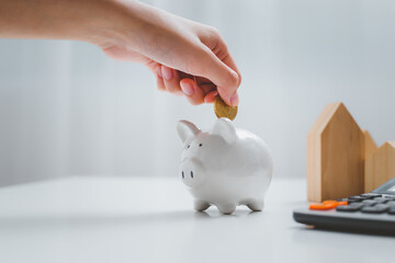 Woman's hand putting coin in piggy bank to save money to buy house.