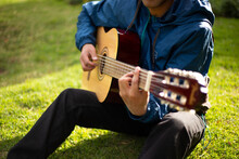 Joven Cantando Y Tocando Guitarra En Un Parque Al Atardecer. Concepto De Personas Y Musica.