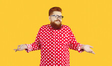 Funny Stylish Bearded Fat Man Who Knows Nothing Or Doubts And Therefore Shrugs Isolated On Orange Background. Red-haired Chubby Man Spread His Arms To Side Shows That He Has No Idea What Is Going On.