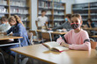 © JackF - Ten-year-old schoolgirl in a protective mask, preparing for lessons in the school library during the pandemic, writes out a ..abstract from a textbook in a exercise book