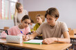 © JackF - Teenager boy and younger girl sitting at desk in classroom and doing tasks.