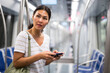 © JackF - Asian woman with shoulder bag standing in subway car and using her smartphone.