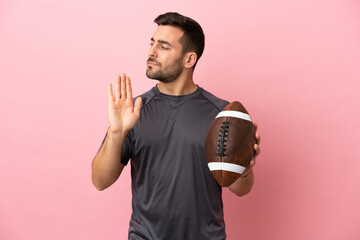 Wall Mural - Young caucasian man playing rugby isolated on pink background making stop gesture and disappointed