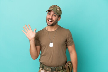 Wall Mural - Military with dog tag over isolated on blue background saluting with hand with happy expression