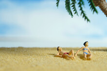 Miniature People Toy Figure Photography. Men And Girl Couple Relaxing, Lying At Beach Sand When Daylight At Seaside