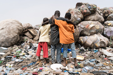 Three young African children standing hopelessy in front of a garbage mountain, symbolizing health hazards and child labor in an African country.