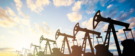 Oil pump jack. Oil industry equipment silhouette against blue sky clouds background