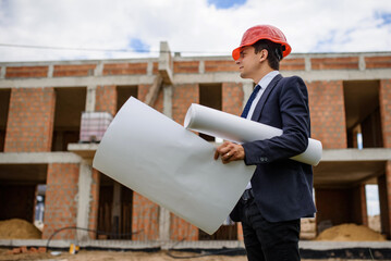 Engineer architect is holding a paper plan of a building at the construction site..