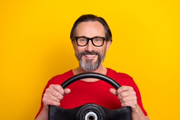 Photo of cheerful pretty retired man wear red t-shirt spectacles riding car smiling isolated yellow color background