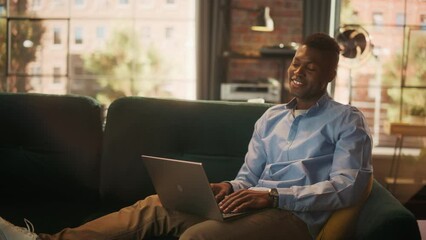 Leinwandbilder - Smiling African American Man Chatting with Friends on Laptop Computer while Sitting on Couch in Stylish Cozy Living Room. Smart Male Communicating with People Using Social Networks