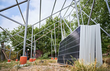 Metal Supporting Structures, Solar Modules For Generating Electricity Through Photovoltaic Effect And Male Workers. Solar Installers Assembling Solar Panel System In Grassy Area With Trees.