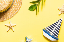 Summer Vacation Concept. Straw Hat, Green Tropic Plant And Beach Decorations On Light Yellow Background With Copy Space For Your Design.