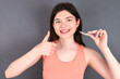 young beautiful Caucasian woman wearing orange T-shirt over grey wall holding an invisible braces aligner and rising thumb up, recommending this new treatment. Dental healthcare concept.