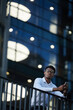 © Mediaphotos - Contemplative young bearded black businessman in white shirt standing on balcony and using gadget, he working late in business company
