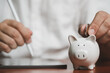 © apiwat - Close up of people hand putting coins in piggy bank for saving money and plan finance. Retirement fund concept.