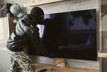 Masked Thief Removes An Expensive TV From The Wall. The Concept Of Apartment Theft