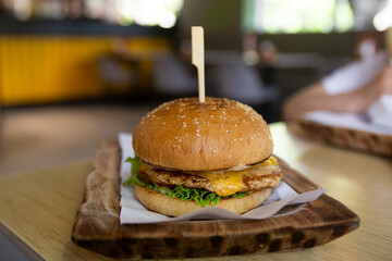 Front view of crispy burger on wooden plate at the fast food cafe.