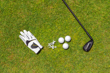 Wall Mural - Top view of golf equipment on green grass on a golf course. Flat lay of golf club, balls, glove, tees