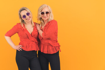 two cheerful Caucasian women with sunglasses posing in front of a camera medium closeup isolated on orange background studio shot . High quality photo