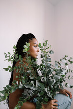 Beautiful Dark-skinned Girl With Black Pigtails On A White Background Posing In Profile On Camera M With A Large Bouquet Of Plants, On Which There Are Many Twigs With Pale Green Leaves