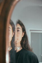 Portrait Of A Girl In The Reflection Of A Mirror With A Wooden Frame In Which Only Half Of Her Face Is Visible
