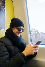 Portrait Of A Guy In A Black Hat And Glasses In A Subway Car Who Laughs While Looking At The Phone