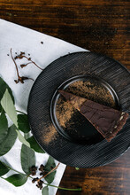 Dark Vegan Cake With Chocolate, On A Black Plate On A Wood Table Decorated With Live Leaves