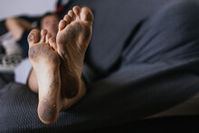 Unrecognizable Man Lying On The Sofa With The Soles Of His Feet Dirty From Walking Barefoot.concept Feet And Personal Hygiene Care.