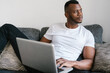 © Ezequiel Giménez/Stocksy - Black man using laptop on sofa