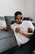 © Ezequiel Giménez/Stocksy - African American male browsing cellphone near couch