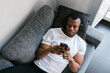 © Ezequiel Giménez/Stocksy - Black meloman using smartphone on couch