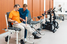 Therapist Helping Man To Exercise On Machine In Rehabilitation Center