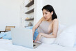 © Roman Shalenkin/Stocksy - Asian woman browsing laptop on bed