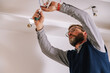 © David Prado/Stocksy - Male electrician installing ceiling illumination